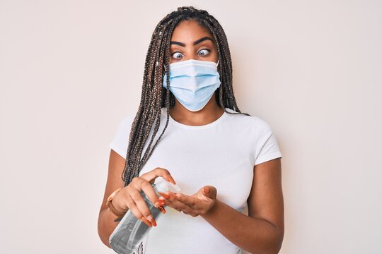 Young african american woman with braids wearing medical mask using hand sanitizer making fish face with mouth and squinting eyes, crazy and comical.