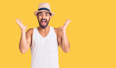Naklejka premium Young hispanic man wearing casual summer hat celebrating crazy and amazed for success with arms raised and open eyes screaming excited. winner concept