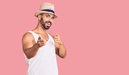 Young hispanic man wearing casual summer hat pointing fingers to camera with happy and funny face. good energy and vibes.