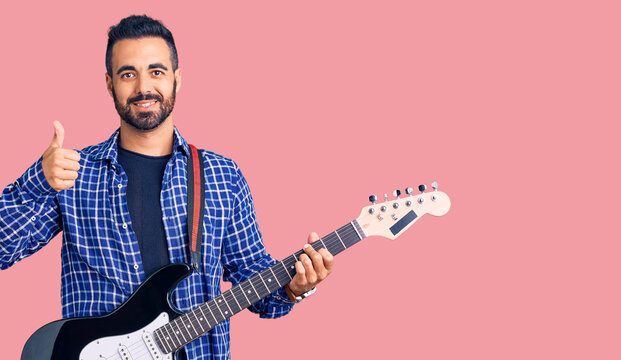 Young hispanic man playing electric guitar smiling happy and positive, thumb up doing excellent and approval sign