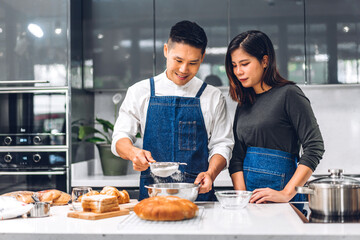 Fototapeta na wymiar Young asian family couple having fun cooking together with baking cookies and cake ingredients on table.Happy couple looking to preparing the dough in kitchen