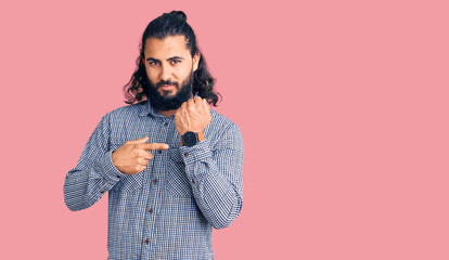 Young arab man wearing casual clothes in hurry pointing to watch time, impatience, looking at the...