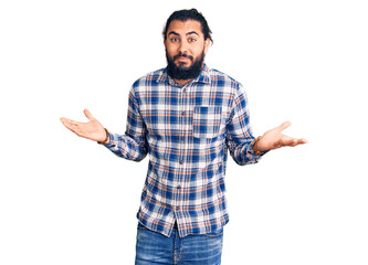 Young arab man wearing casual clothes clueless and confused expression with arms and hands raised....