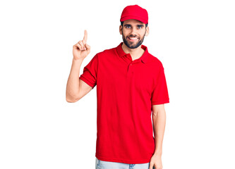 Young handsome man with beard wearing delivery uniform showing and pointing up with finger number one while smiling confident and happy.