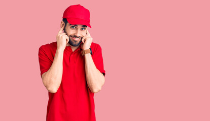 Young handsome man with beard wearing delivery uniform covering ears with fingers with annoyed expression for the noise of loud music. deaf concept.