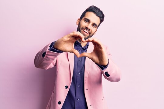 Young handsome man with beard wearing elegant jacket smiling in love doing heart symbol shape with hands. romantic concept.