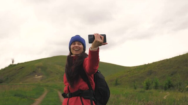 free Young girl tourist blogger records selfie videos at foot of mountains using a smartphone with beautiful landscape in background. Healthy cheerful woman travels and photography nature by phone