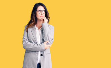 Beautiful young brunette woman wearing business clothes and glasses serious face thinking about...