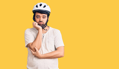 Young hispanic man wearing bike helmet thinking looking tired and bored with depression problems with crossed arms.