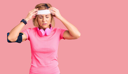 Obraz na płótnie Canvas Young blonde woman wearing sportswear and headphones suffering from headache desperate and stressed because pain and migraine. hands on head.