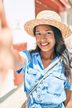 Young beautiful indian woman wearing summer hat smiling happy making selfie by the camera at the city.