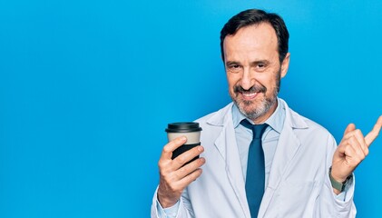 Middle age handsome doctor man wearing coat drinking cup of takeaway coffee smiling happy pointing with hand and finger to the side