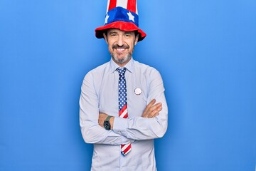 Middle age handsome patriotic man wearing united states hat and tie over blue background happy face smiling with crossed arms looking at the camera. Positive person.
