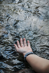 Hands touch in flowing water from the river in nature outdoors on a sunny warm day,