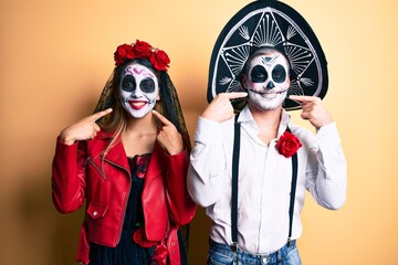 Couple wearing day of the dead costume over yellow smiling cheerful showing and pointing with fingers teeth and mouth. dental health concept.