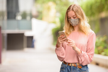 Obraz premium Young blonde woman with mask using phone in the city with nature