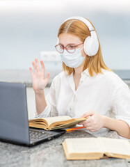 Fototapeta na wymiar Young girl wearing medical protective mask uses laptop at home. Distance learning. Quarantine and coronavirus epidemic concept