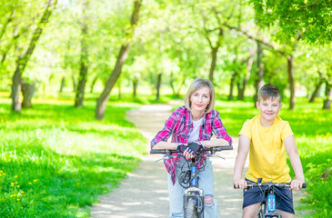 Portrait of a mother and son standing with bicycles in sunny summer park. Empty space for text