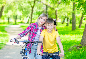 Obraz premium Sporty family leisure. Happy mother embraces her young son, who ride bikes in a summer park