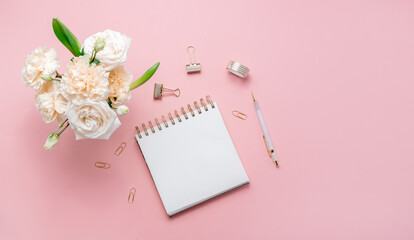 Stationery business flatlay creative composition. Top horizontal view of envelope, spiral blocj paper clips and a pen on abstract pink background.
