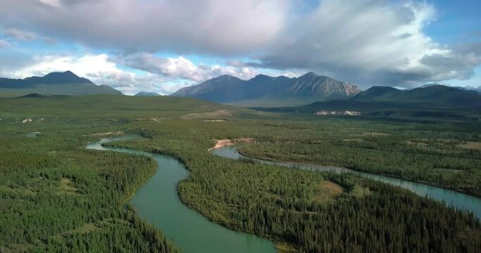 Breathtaking summer Yukon scenic backward flight above Takhini curvy river by evergreen tree forest in Ibex valley with epic view of majestic Mount Ingram, Canada, overhead aerial pull back