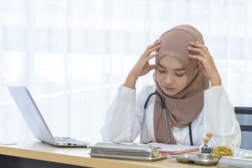 Young Asian woman Muslim doctor wearing hijab keeps hands on temples feeling fatigue and tired