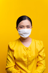 Asian woman wearing protective face mask isolated on yellow background.