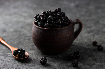 Fototapeta na wymiar Blackberries in an earthenware mug are piled with a hill. Next to it is a wooden spoon in which the berries are scattered around on the table