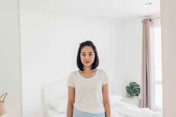 Fototapeta na wymiar Straight portrait of Asian woman standing in white bedroom.