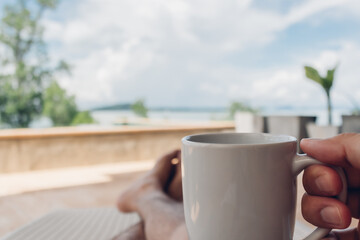 Man drinks coffee on the balcony by the sea in concept of relaxation and vacation.