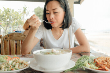 Asian woman in white t-shirt is eating Tom Yam Seafood.