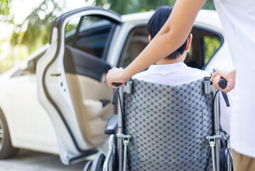 Caregiver helping senior handicapped asian woman from wheelchair get into car