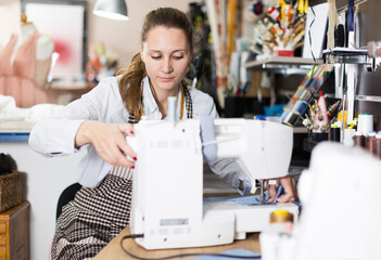 Young female tailor working with sewing machine at workshop