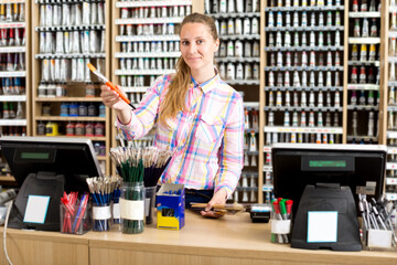 Cheerful young female seller posing at counter in art store