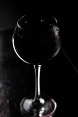 Large silhouette of a glass on a black background, with a red drink inside. A drop falls from above