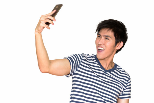 Studio shot of young happy Asian man taking selfie with mobile phone isolated against white background