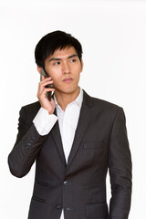 Studio shot of young handsome Asian businessman talking on mobile phone isolated against white background