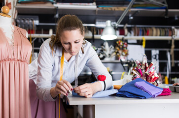 Positive woman worker sew up textile material at sewing workshop