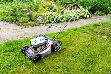 Old petrol lawnmower on the background of the lawn and flowers