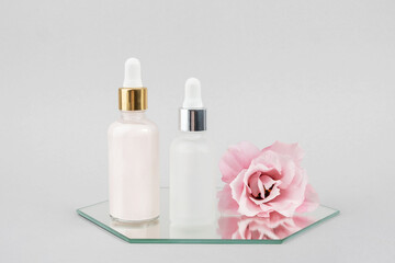 Fototapeta na wymiar Two glass bottles with serum, essential oil or other cosmetics product and beautiful pink flowers on mirror on grey background. Natural Organic Spa Cosmetic Beauty concept Front view