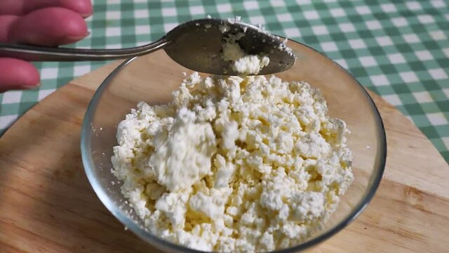 Cottage cheese on plate with a spoon at background wooden board