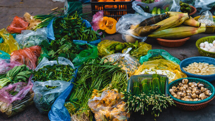 On the sidewalk at a local market in Vietnam, a lot of vegetables at one stand such as eggplant, papaya, lettuce, eggs, bamboo shoots, bitter melon, corn, tomatoes, cucumbers ...