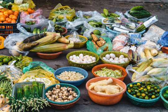 On the sidewalk at a local market in Vietnam, a lot of vegetables at one stand such as eggplant, papaya, lettuce, eggs, bamboo shoots, bitter melon, corn, tomatoes, cucumbers ...
