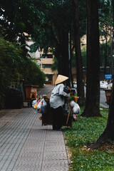 Vietnamese women wearing Non la, street vendors, selling souvenirs and miscellaneous goods, walking on the sidewalk, viewed from behind on street in Saigon