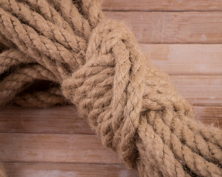 Coiled hemp shibari rope on wooden background with ends and bight locked with tuck under wraps