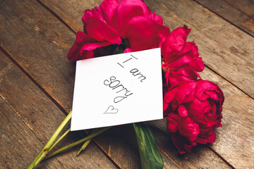 Flowers and paper sheet with text I AM SORRY on wooden background