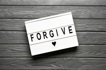 Board with word FORGIVE on wooden background