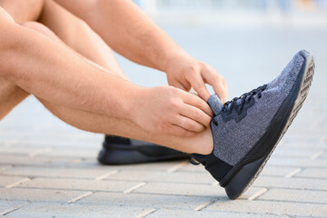 Sporty young man tying shoelaces outdoors, closeup