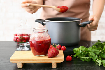 Woman making sweet strawberry jam in kitchen
