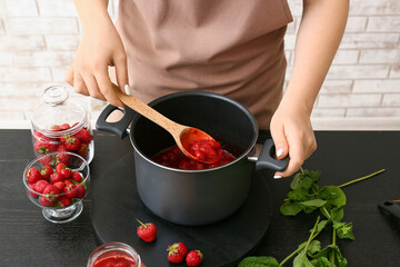 Woman making sweet strawberry jam in kitchen